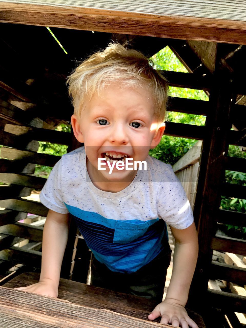 Portrait of cheerful boy playing in wooden jungle gym at playground