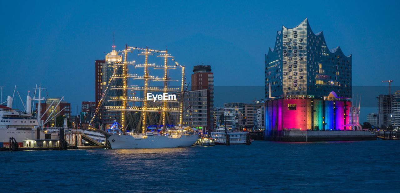 Illuminated city by sea against clear blue sky