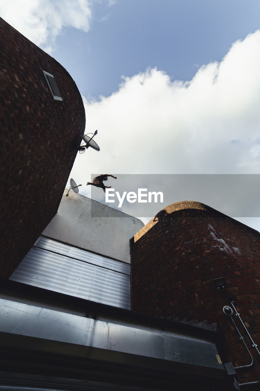 Low angle view of building against sky, man jumping on rooftop