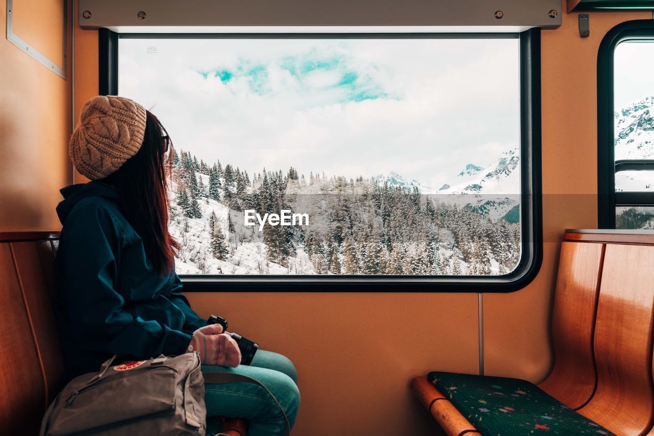 REAR VIEW OF MAN SITTING ON TRAIN WINDOW