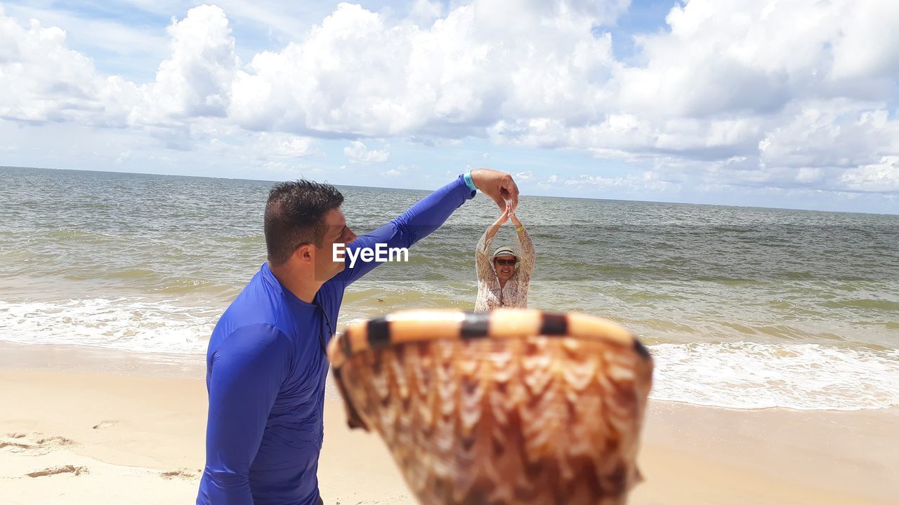 Optical illusion of man removing woman from shell at beach against sky