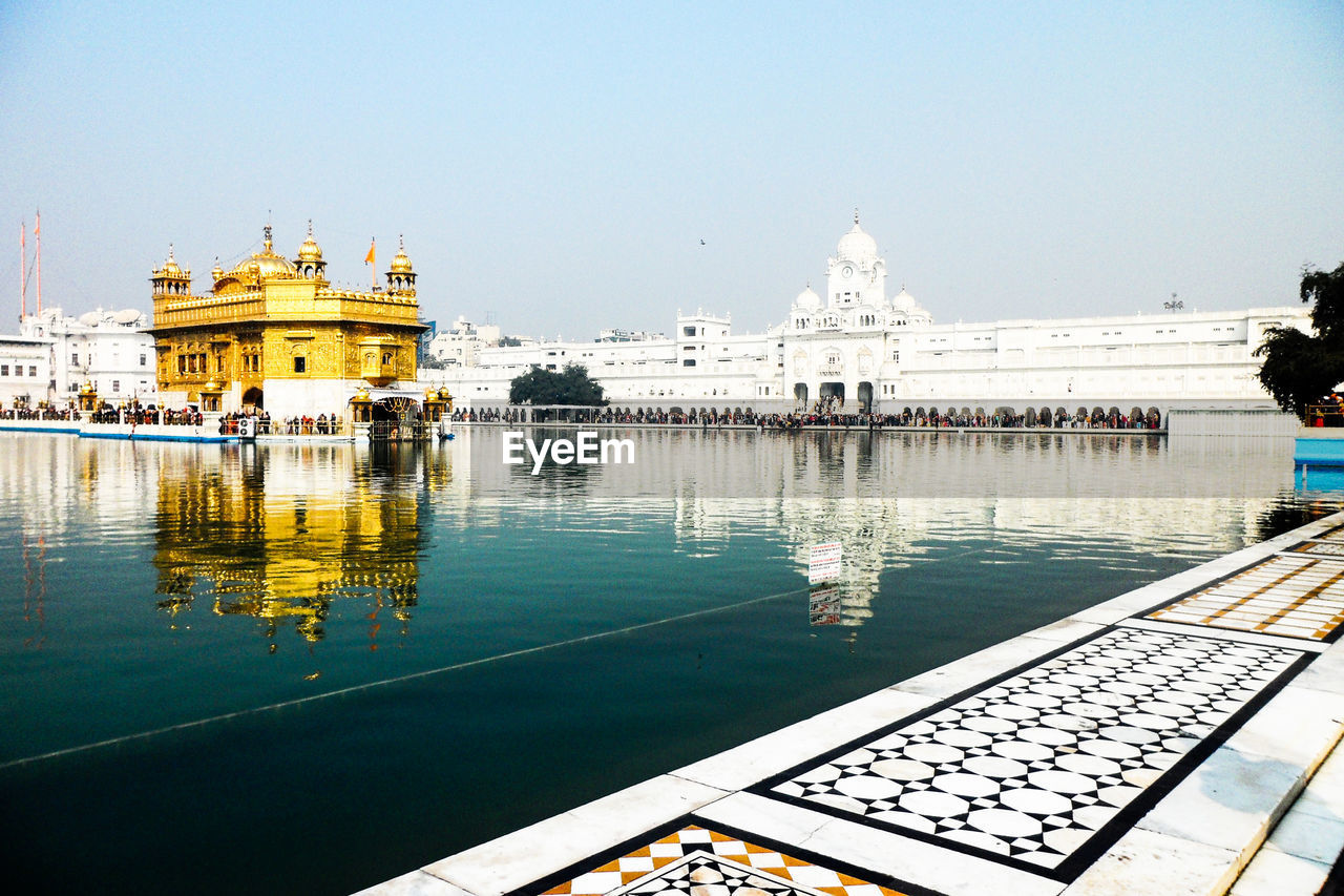 Golden temple by lake against sky