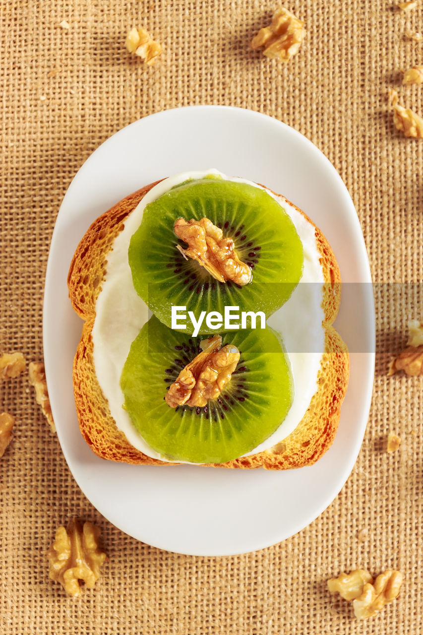 Toast with kiwi, cheese and walnuts on a piece of sackcloth with walnuts around. view from above