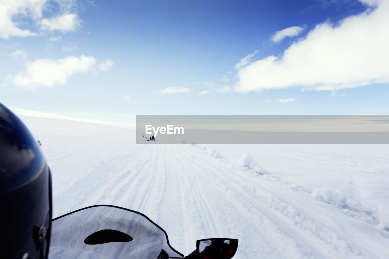 Cropped image of person riding snowmobile on landscape against sky