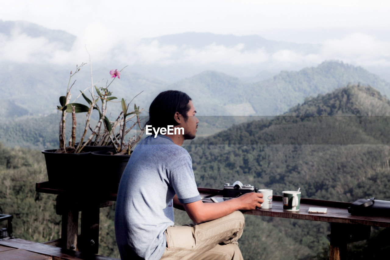 SIDE VIEW OF YOUNG MAN LOOKING AT MOUNTAIN