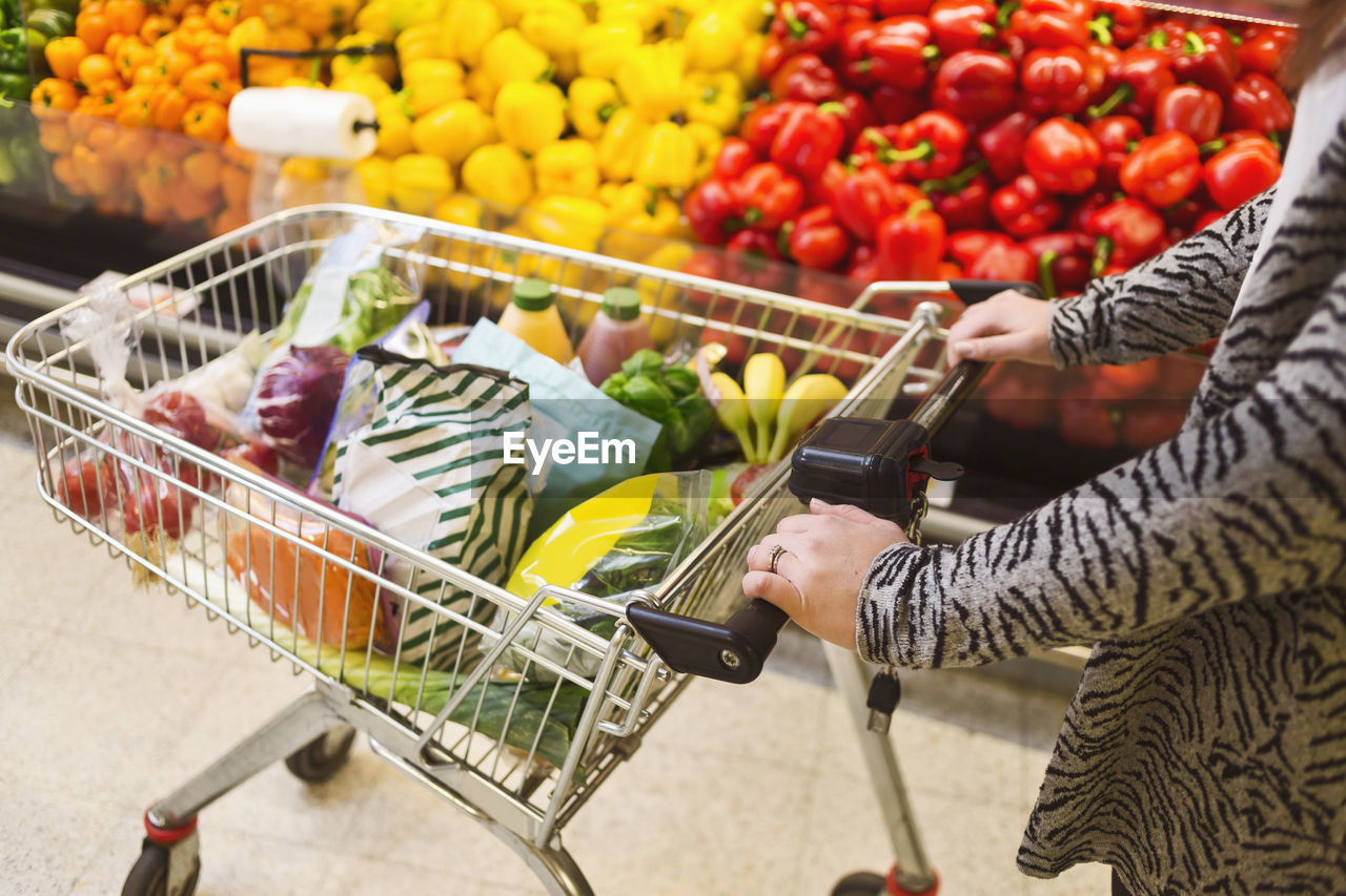 Midsection of woman pushing groceries in shopping cart at supermarket