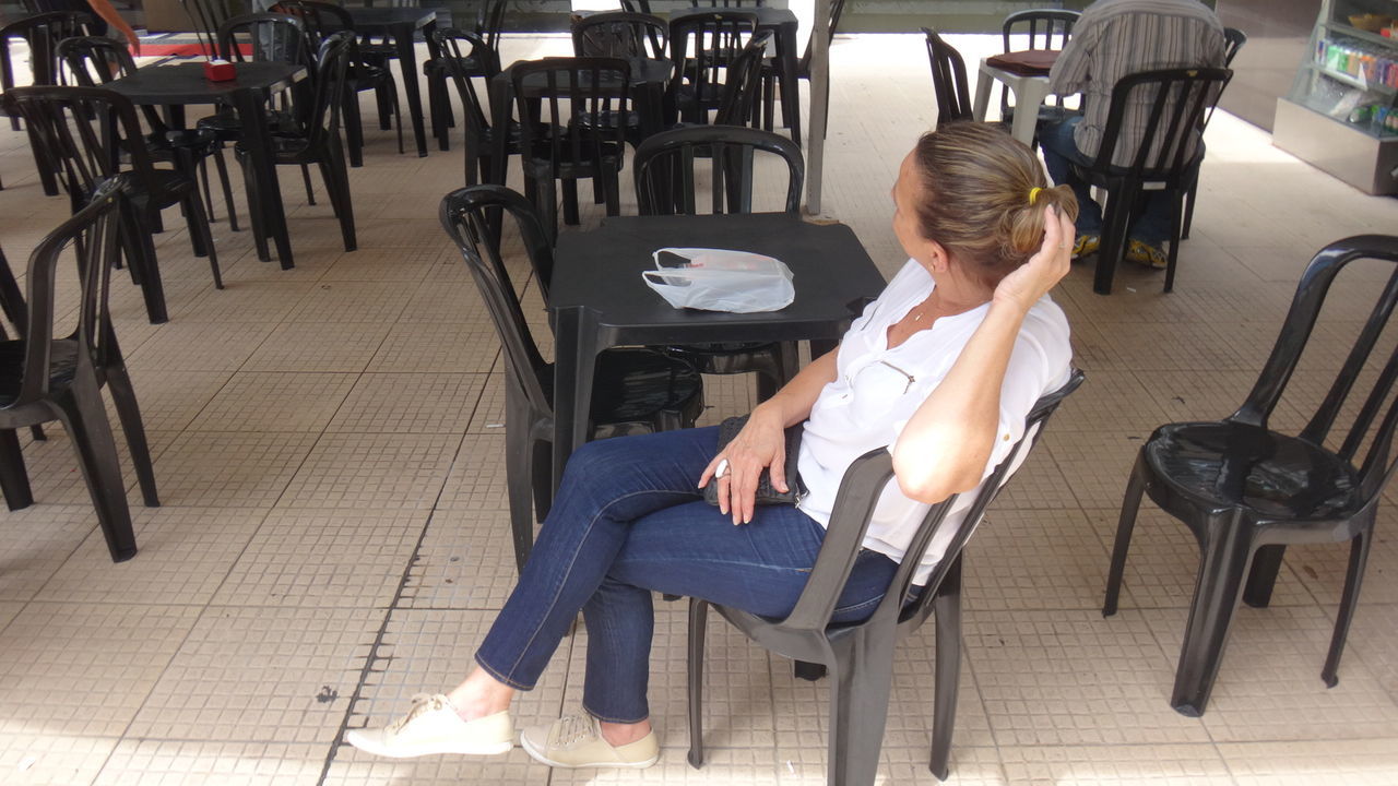 Side view full length of woman sitting on chair at cafe