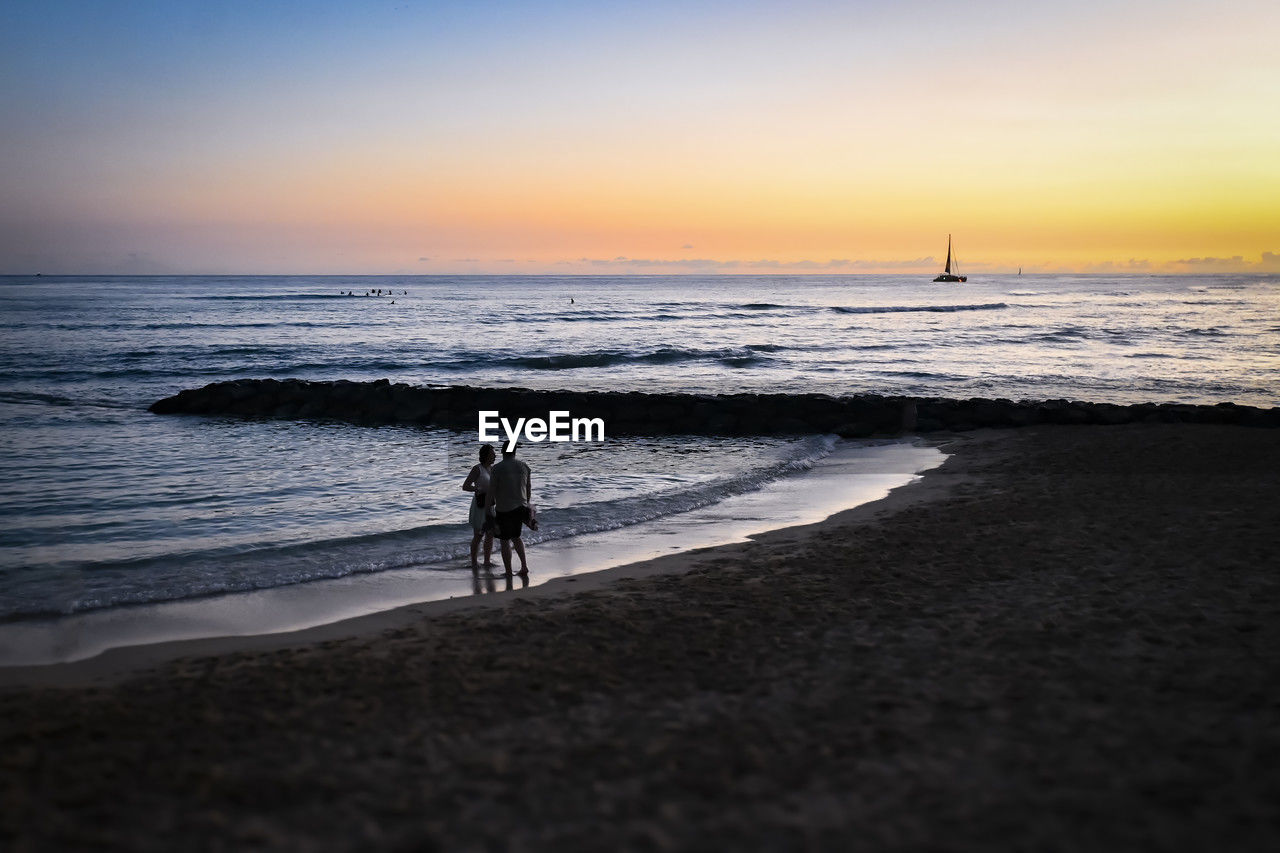 sea, water, beach, sky, land, horizon, ocean, sunset, wave, body of water, shore, coast, beauty in nature, nature, horizon over water, sand, motion, scenics - nature, silhouette, wind wave, men, tranquility, holiday, vacation, leisure activity, sports, trip, full length, lifestyles, adult, tranquil scene, two people, cloud, dawn, walking, outdoors, travel, sunlight, idyllic, transportation, orange color, travel destinations, evening, sun, coastline, activity, reflection