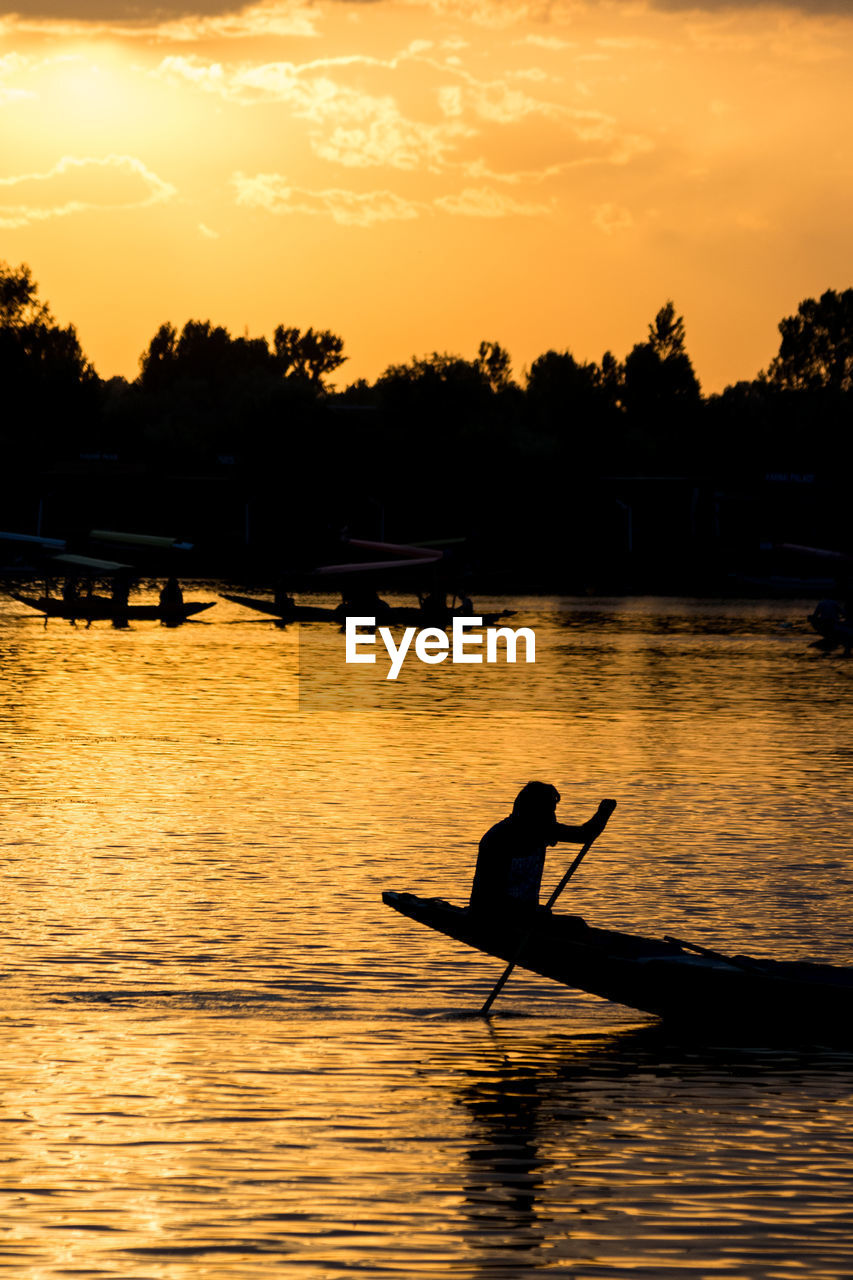 SILHOUETTE MAN ON BOAT AGAINST ORANGE SKY