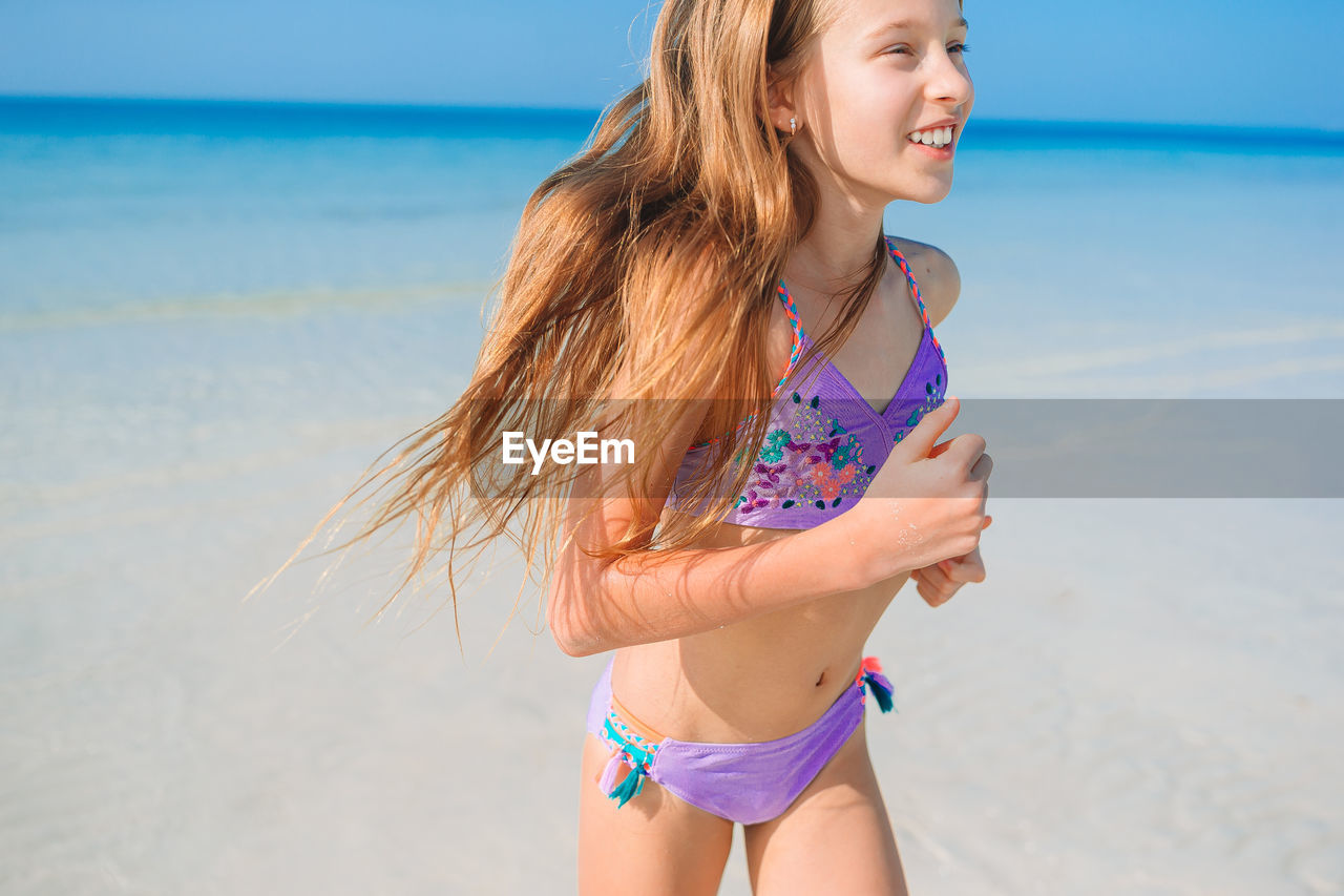 Smiling girl wearing bikini running in beach