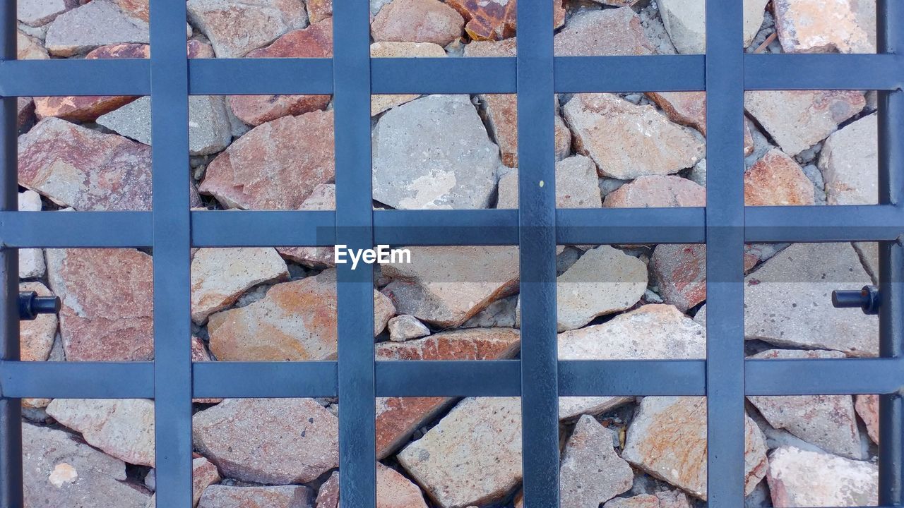 Close-up of metal gate against stones