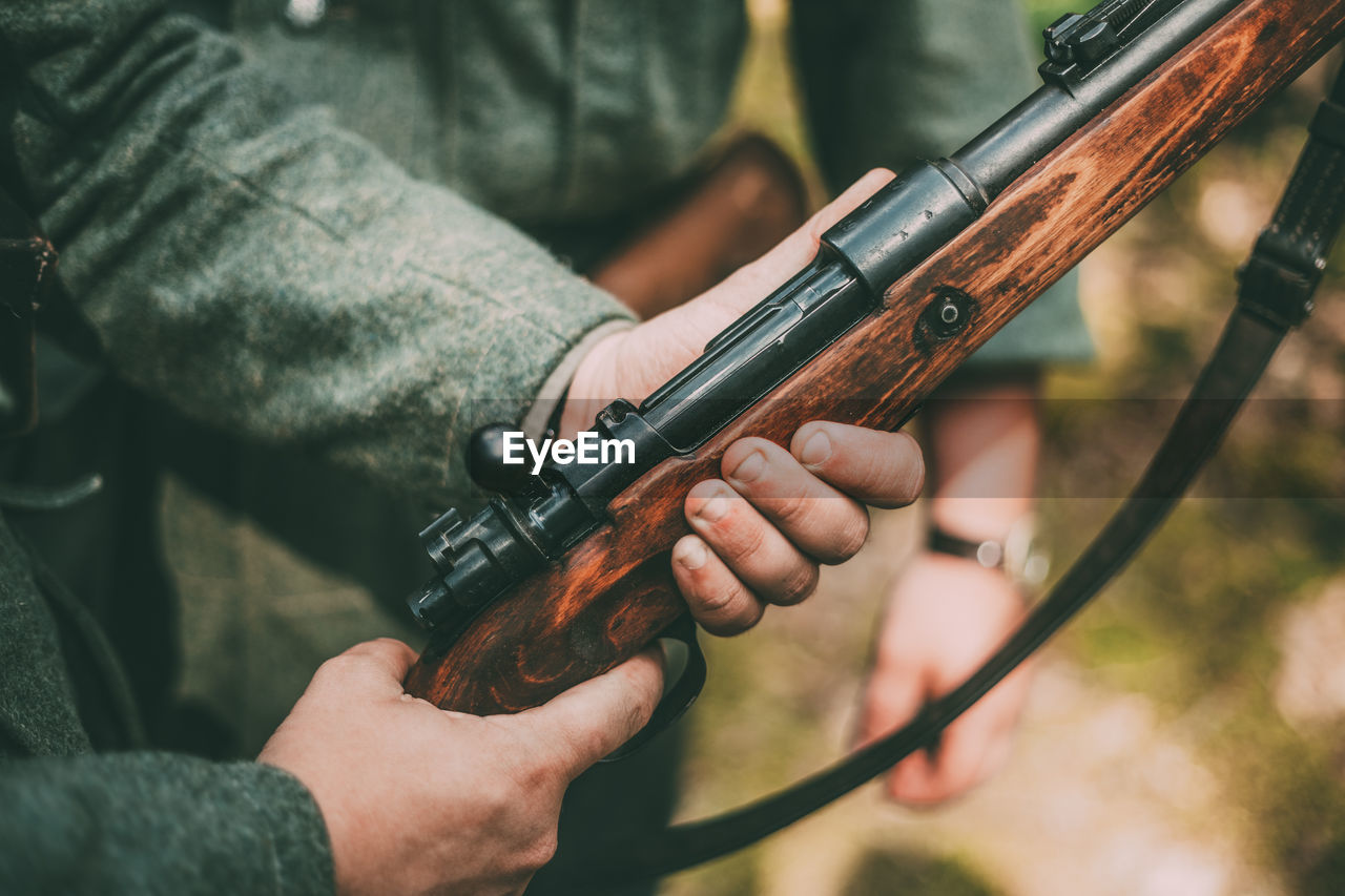 Midsection of army soldier holding gun while standing outdoors