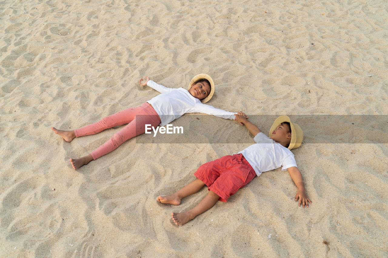 High angle view of siblings lying on sand at beach