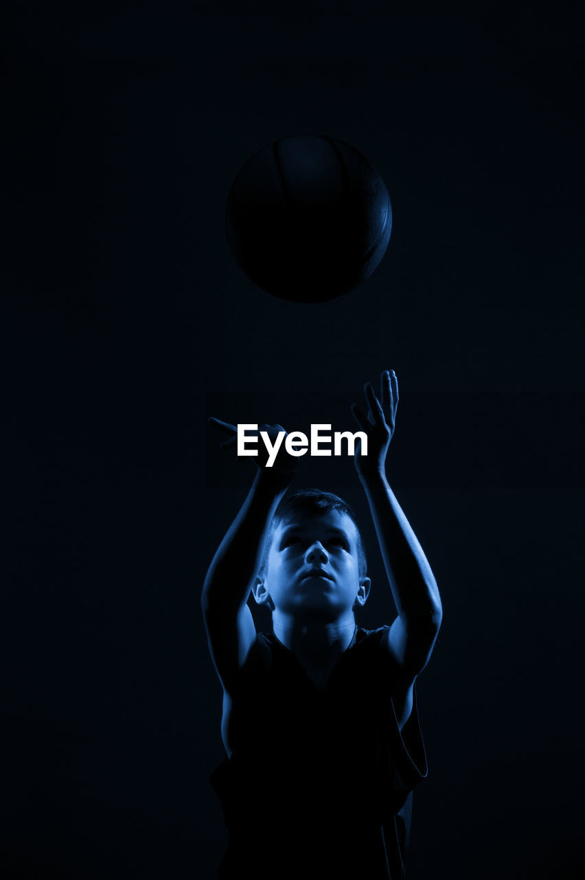 Close-up of boy holding volleyball against black background