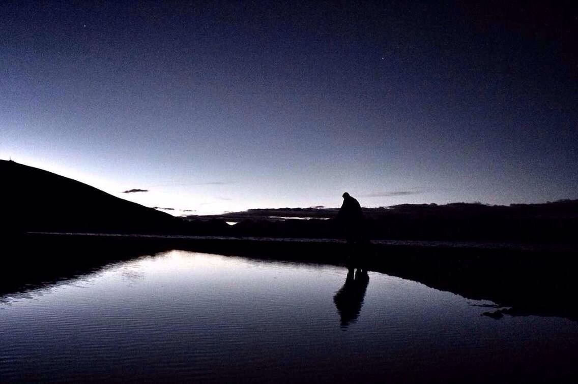 Silhouette man by lake against sky