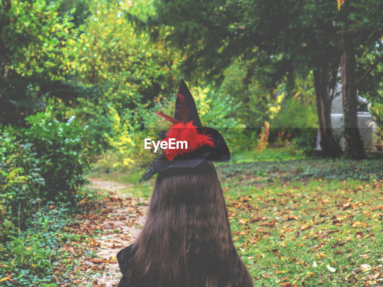 Rear view of woman wearing hat and standing at field amidst trees