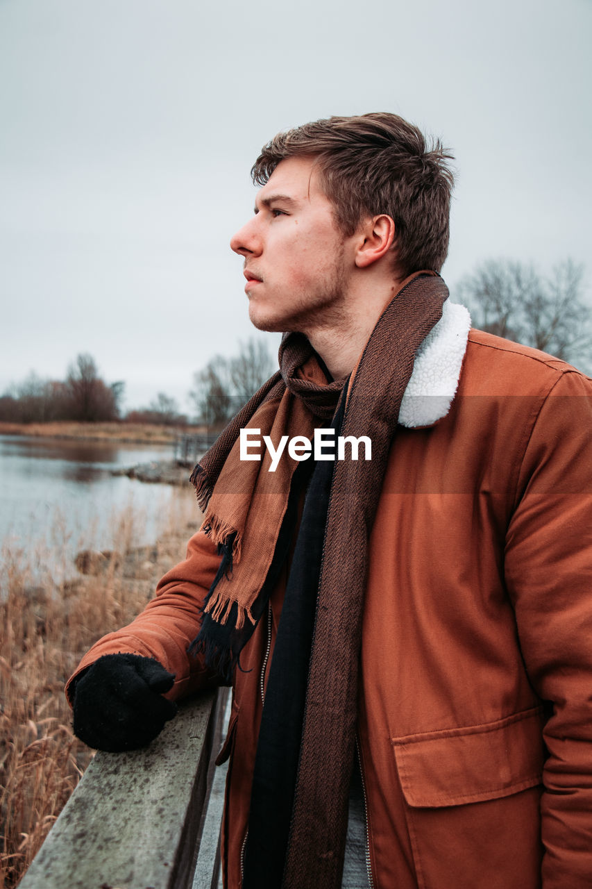 Young man looking away while standing by railing