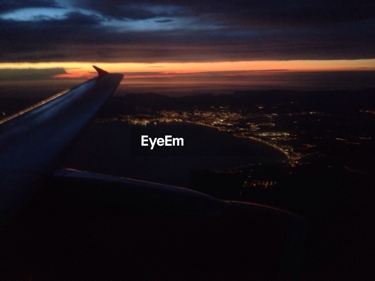 Cropped image of airplane flying over illuminated cityscape