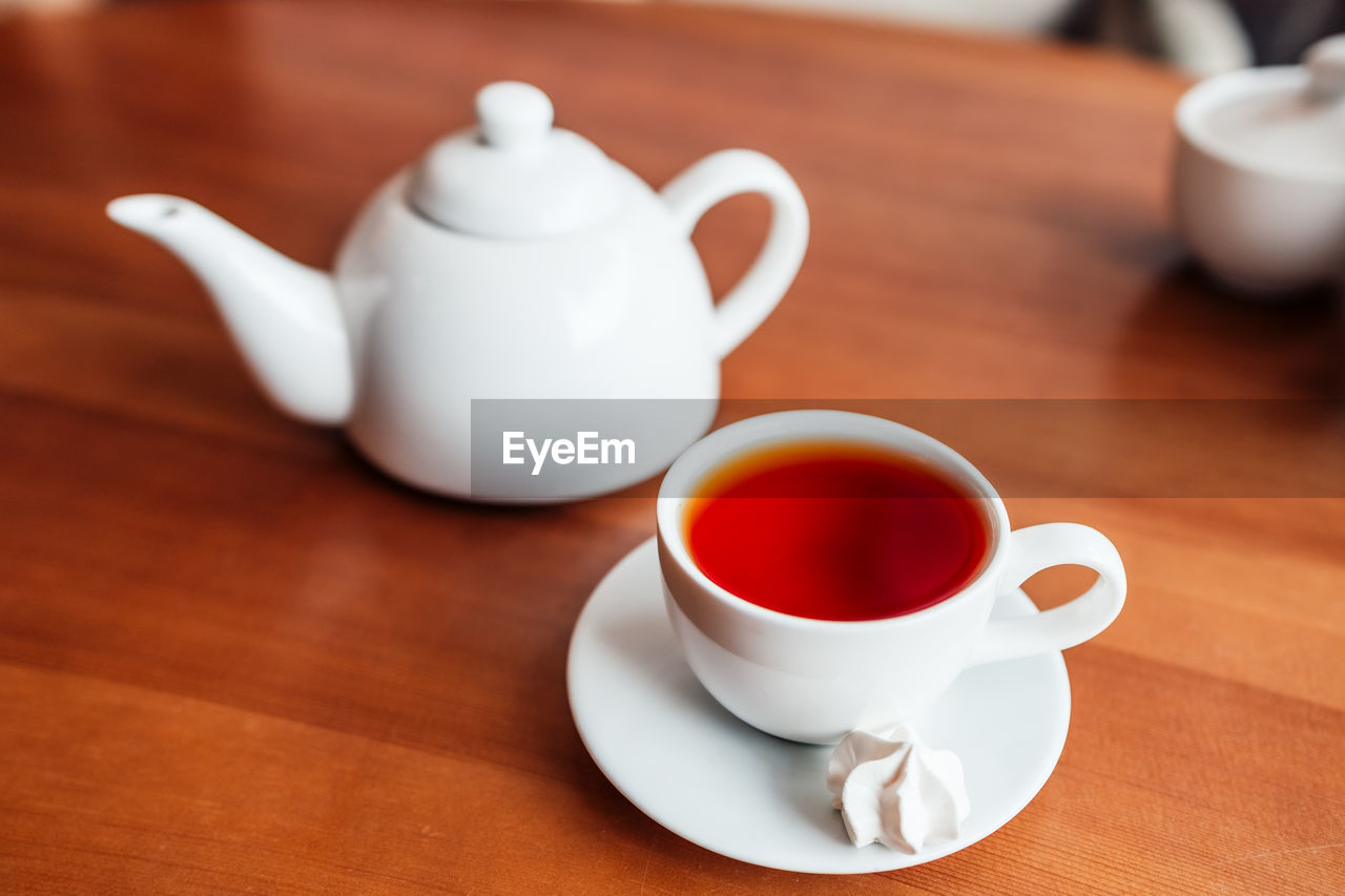 Hot tea in white cup and teapot on table in cafe