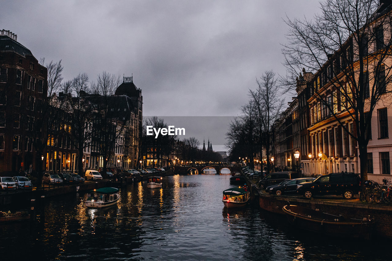 CANAL AMIDST ILLUMINATED CITY BUILDINGS AGAINST SKY