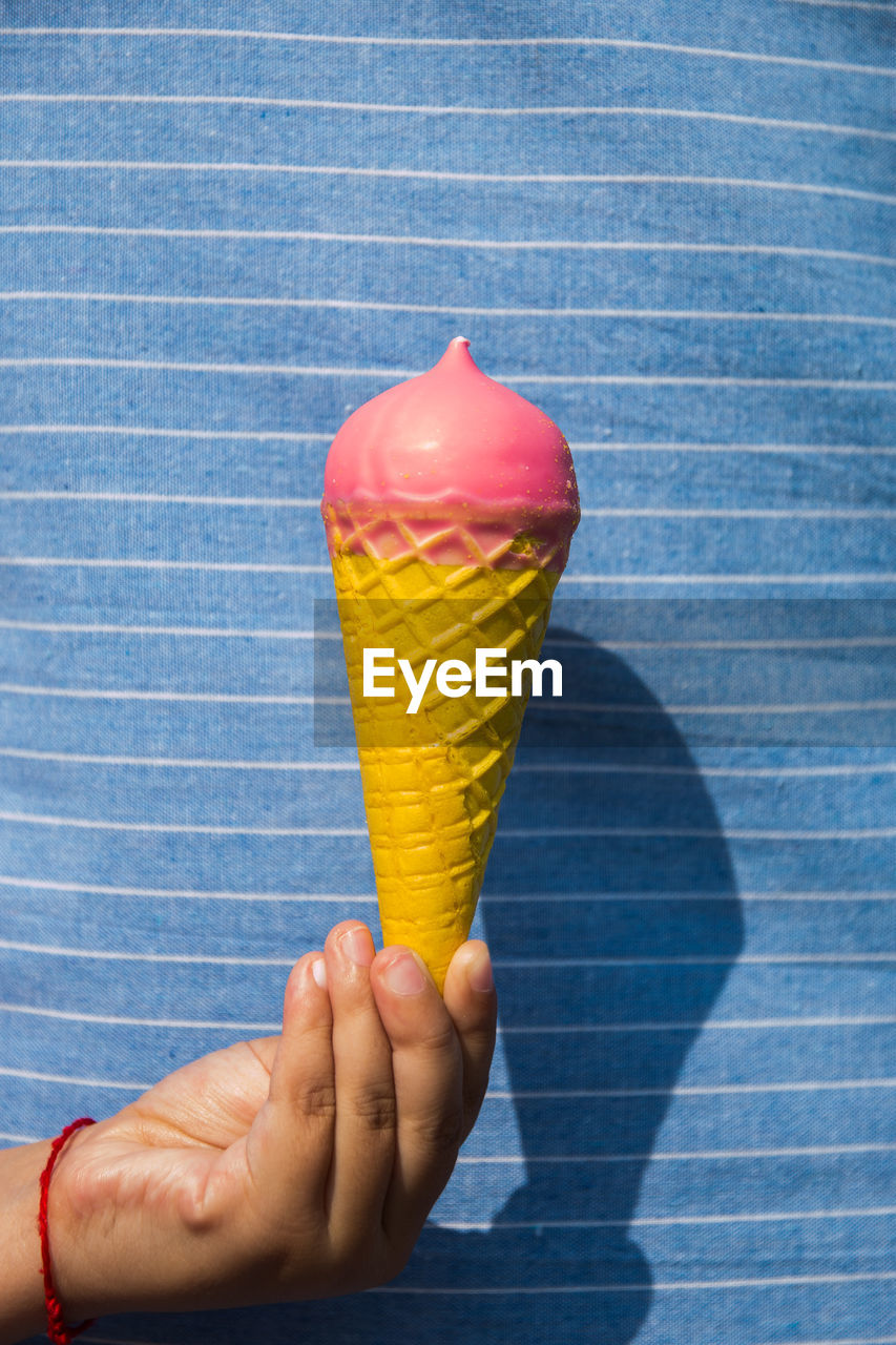 CLOSE-UP OF HAND HOLDING ICE CREAM CONE AGAINST BLUE BACKGROUND