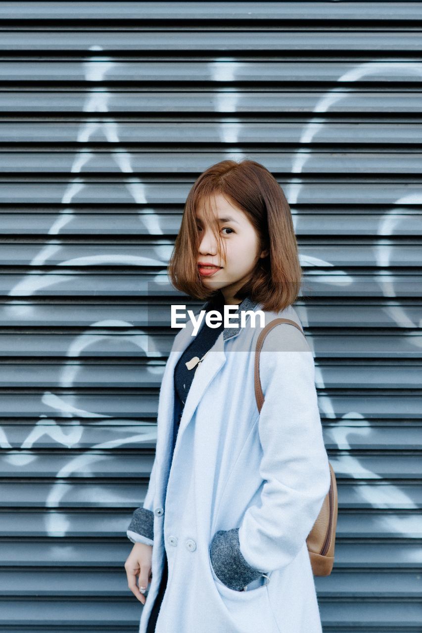 Portrait of young woman standing by shutter