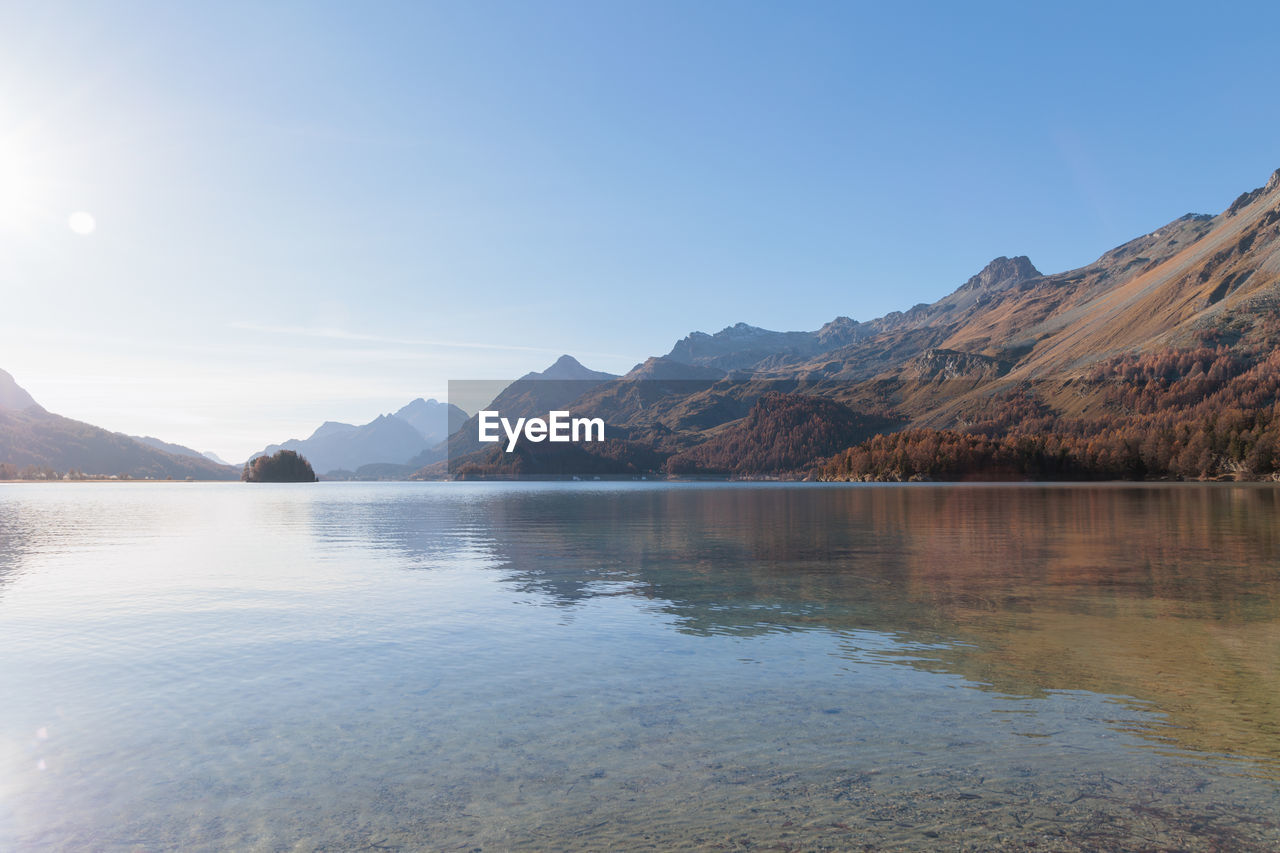 mountain, water, scenics - nature, lake, sky, environment, reflection, beauty in nature, landscape, mountain range, nature, reservoir, body of water, tranquility, tranquil scene, land, travel destinations, no people, travel, clear sky, blue, outdoors, sunny, day, sunlight, wilderness, non-urban scene, copy space, tourism, idyllic, highland, mountain peak