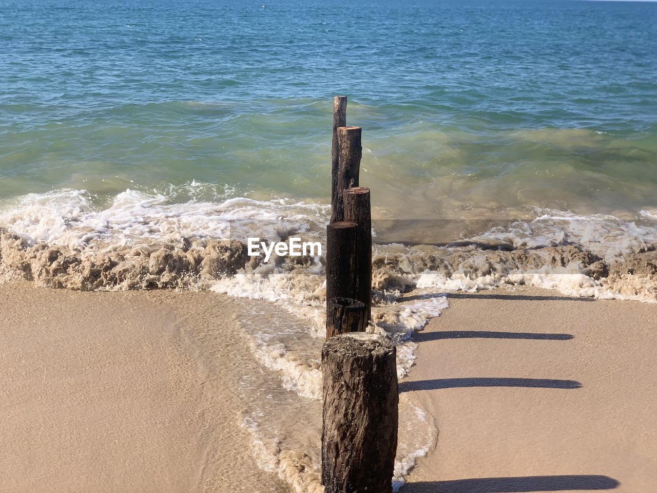 WOODEN POST ON BEACH AGAINST SEA