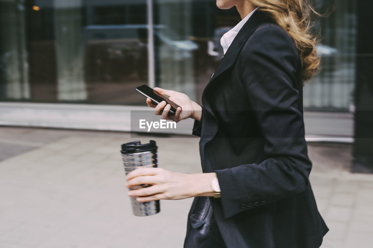 Midsection of businesswoman with coffee mug and phone in city