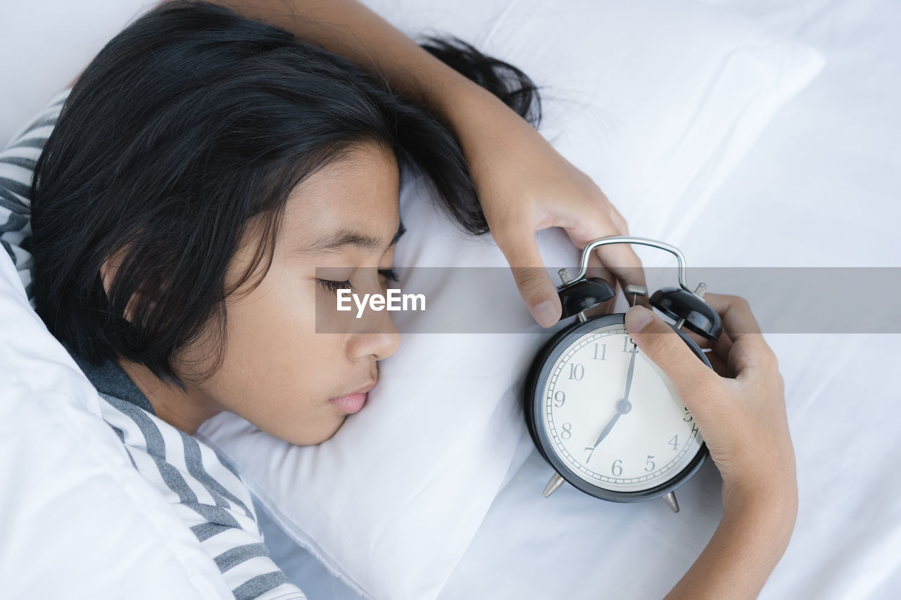 High angle view of girl with alarm clock sleeping on bed