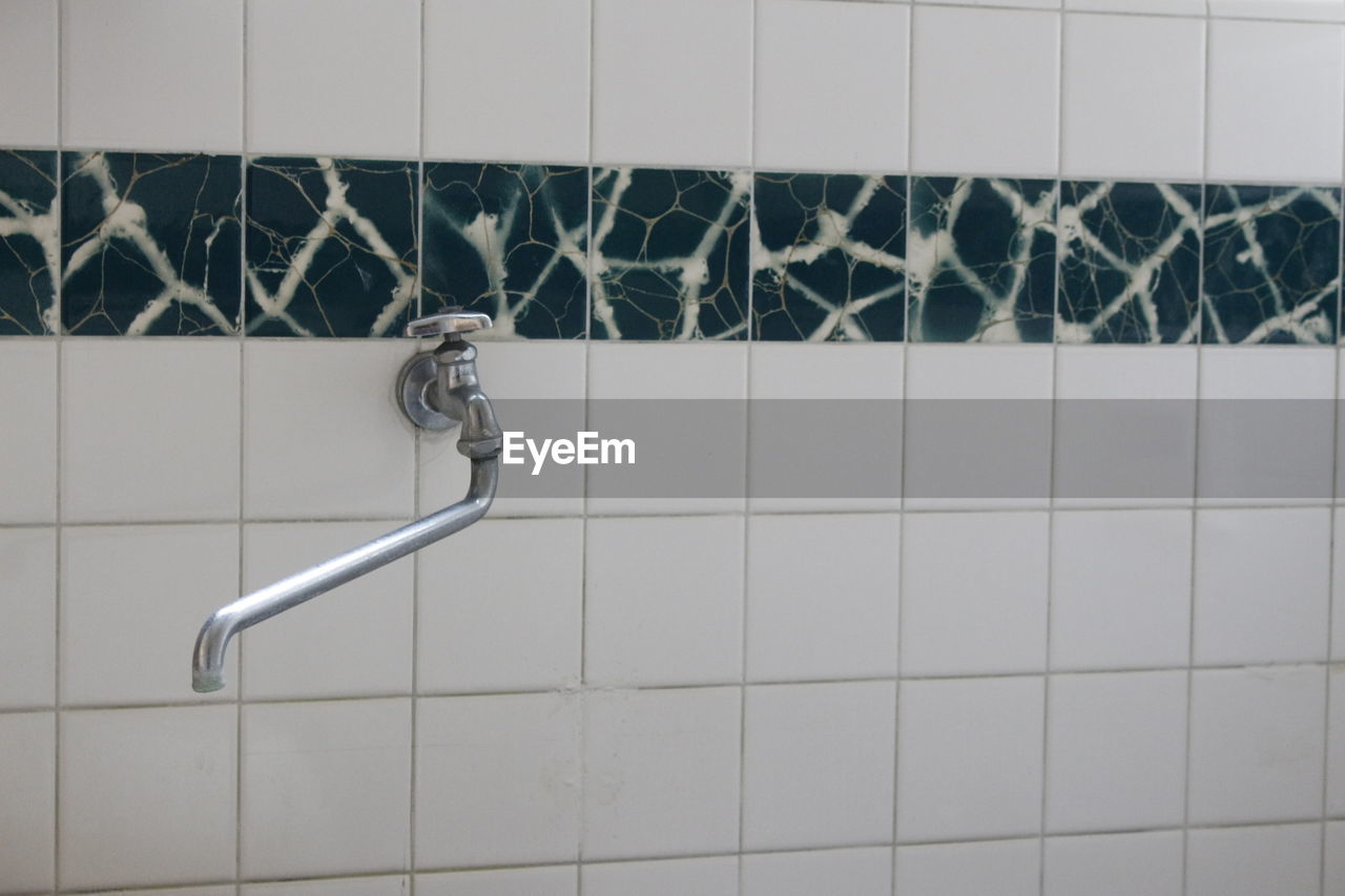 CLOSE-UP OF FAUCET ON TILED WALL AT HOME