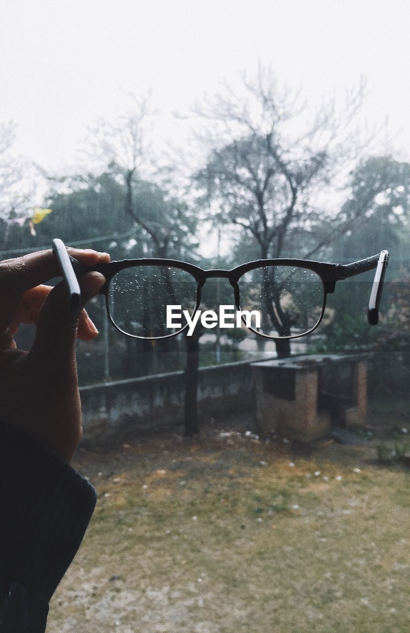 Close-up of hand holding eyeglasses against tree