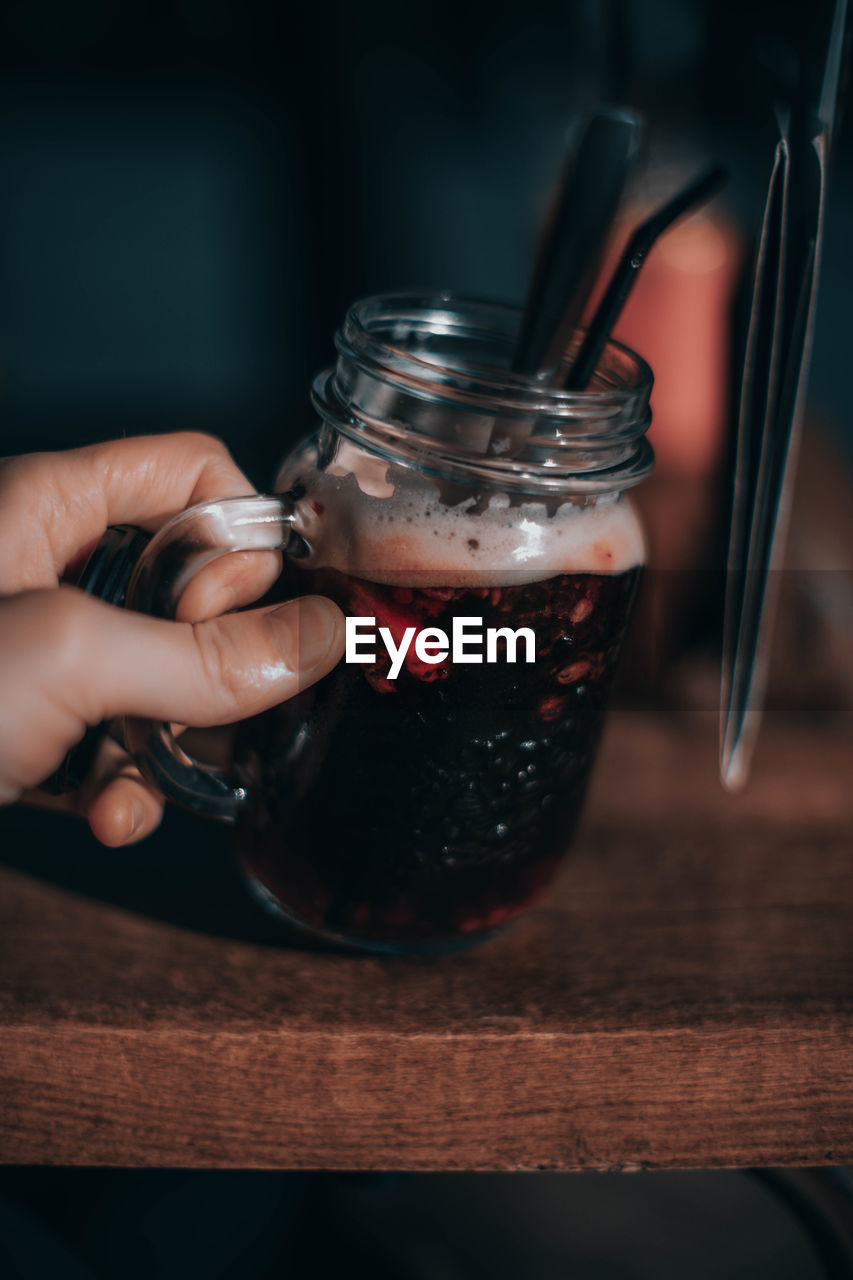 Cropped hand holding drink jar on table