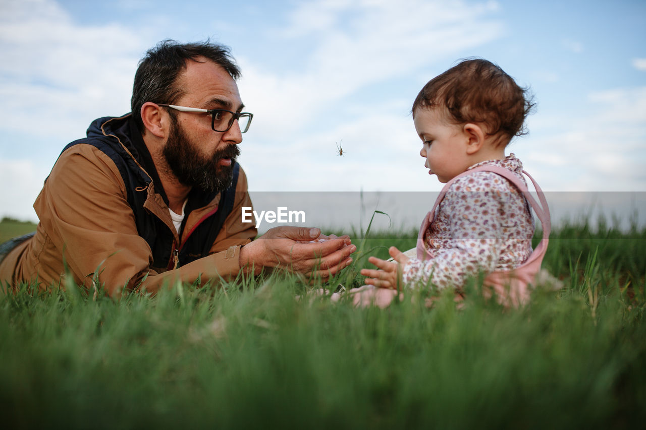 Father and daughter on grass against sky