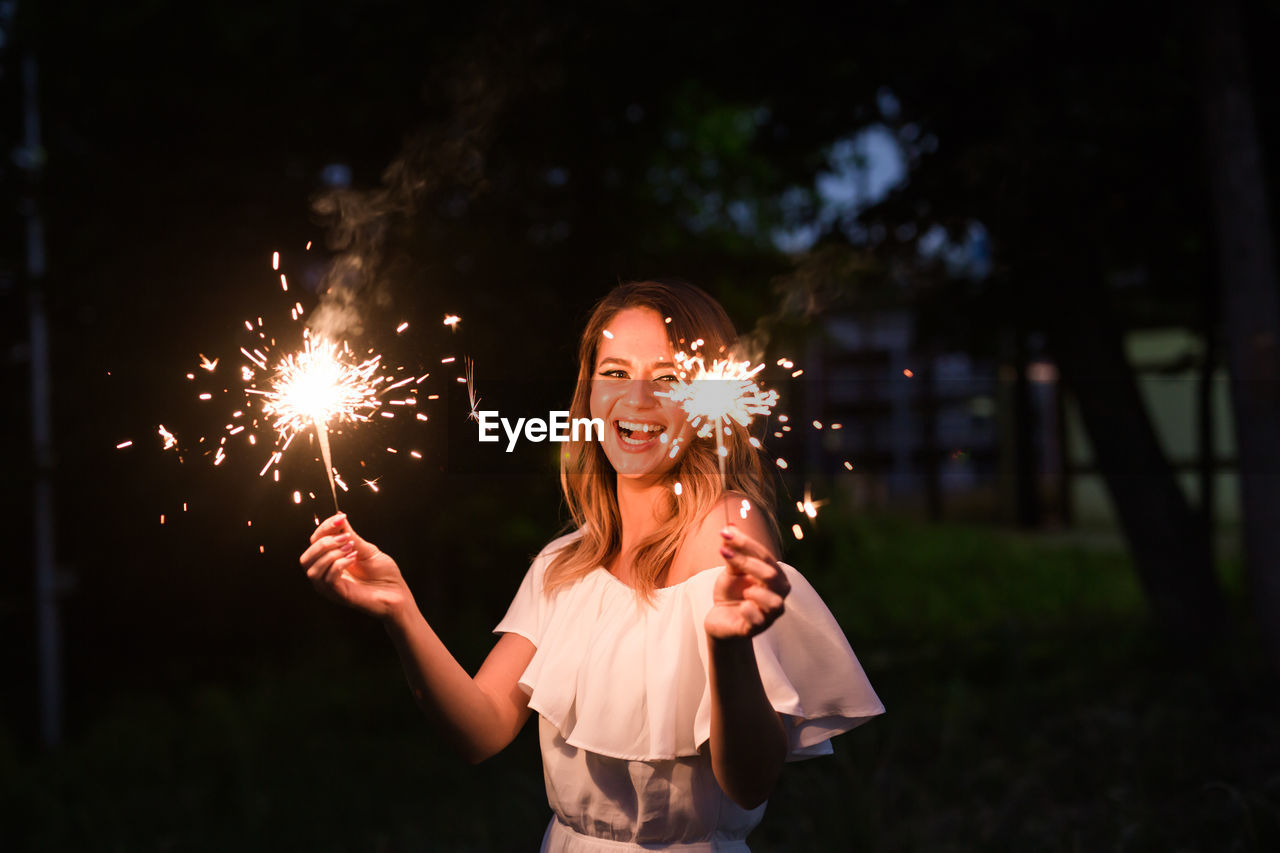 Smiling woman with sparklers at night