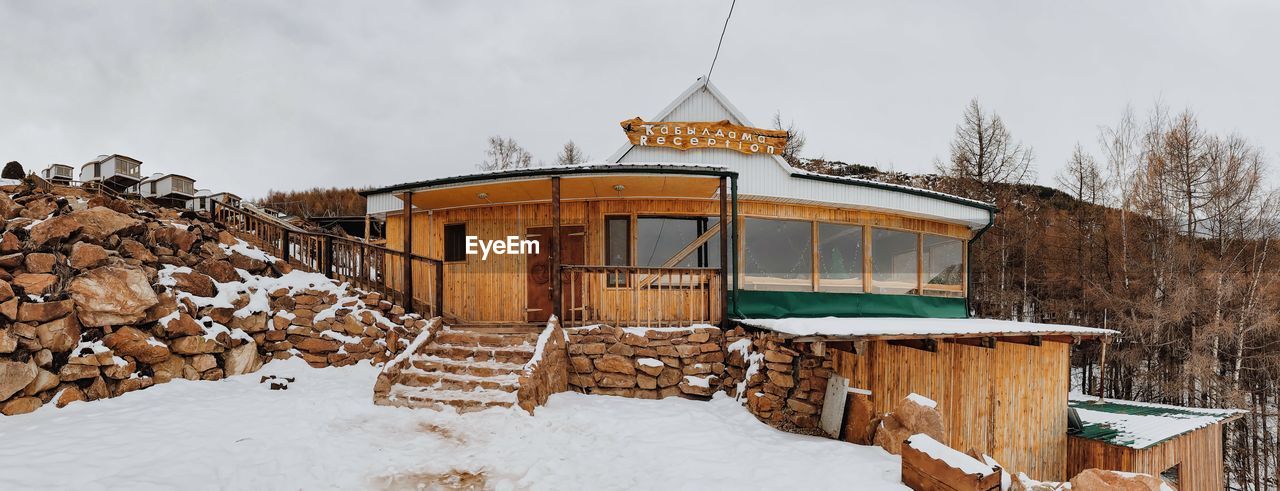 HOUSE ON SNOW COVERED FIELD BY HOUSES AGAINST SKY