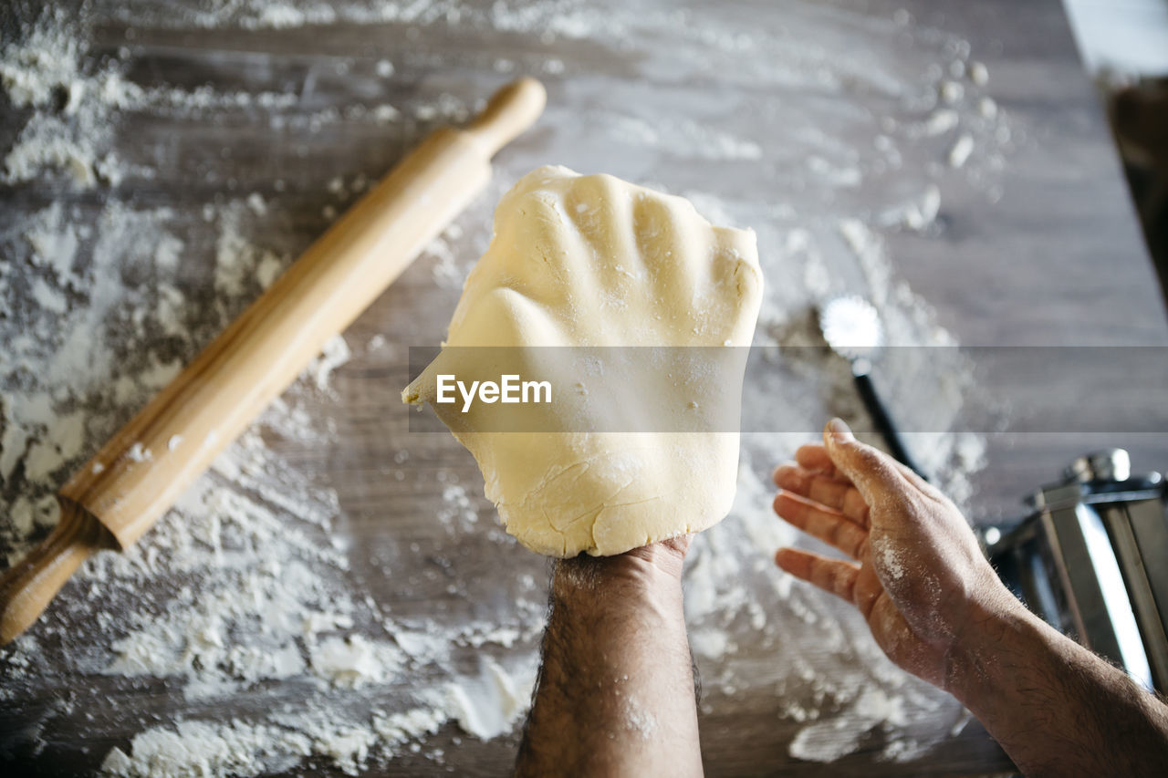 Cropped hands of man holding dough in kitchen