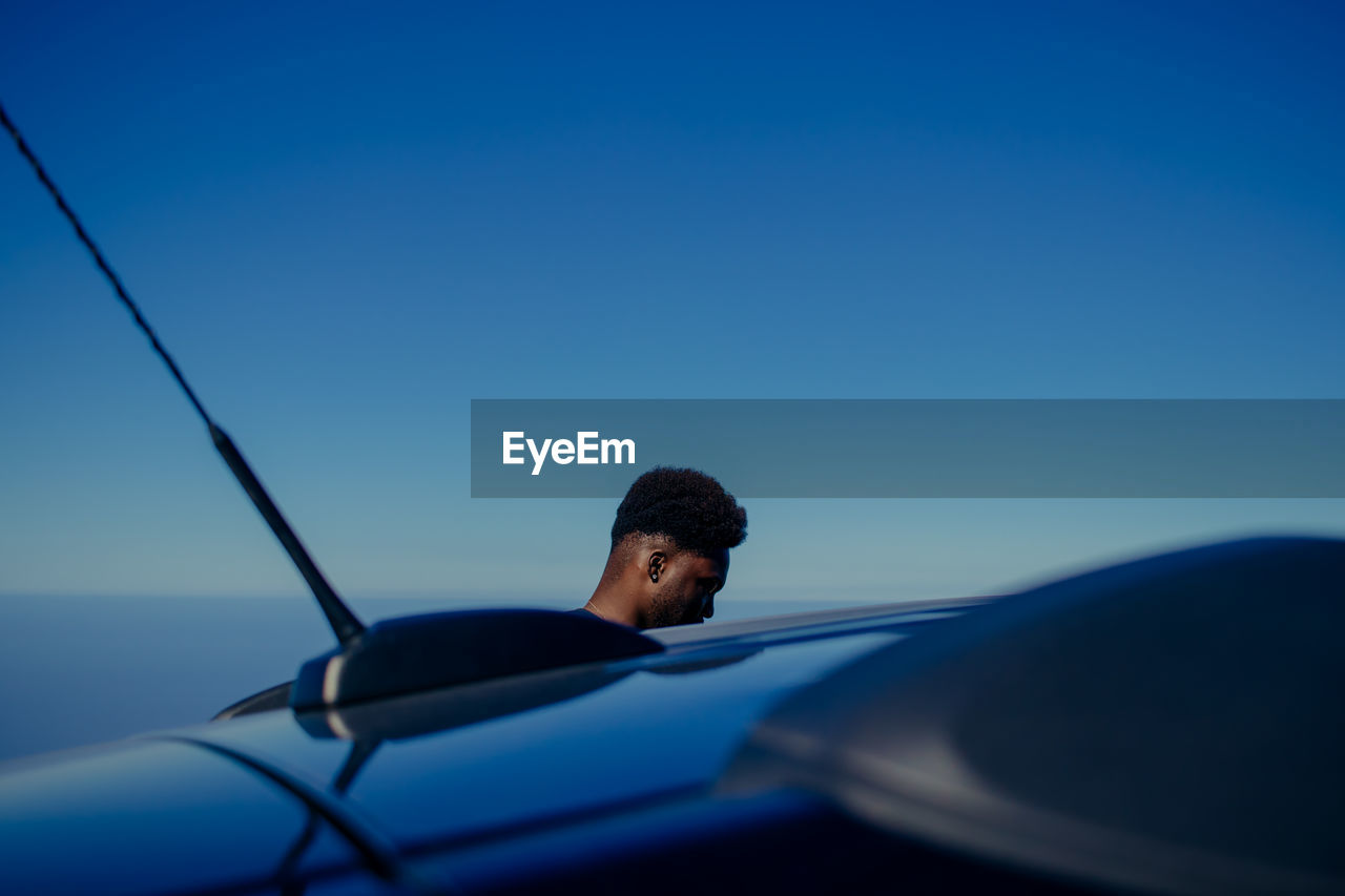 Man by car against blue sky