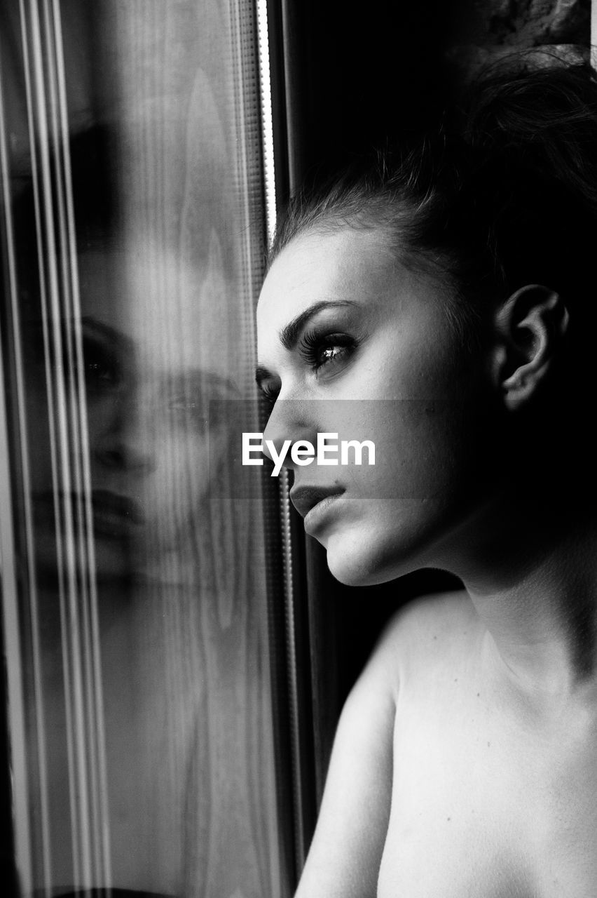 Close-up of woman looking through window at home