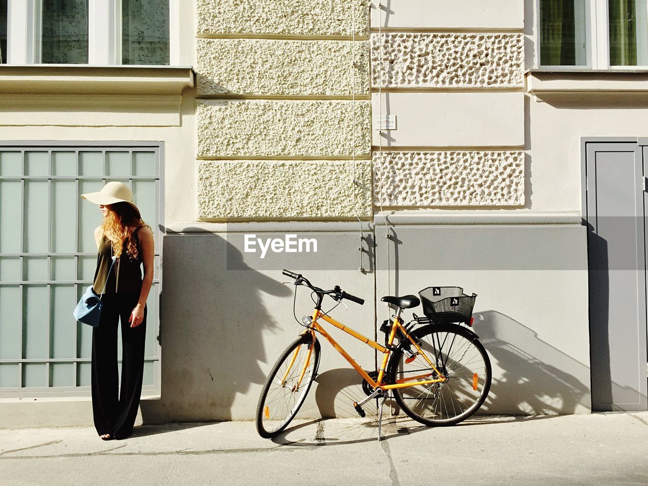 Young woman standing besides bicycle against building
