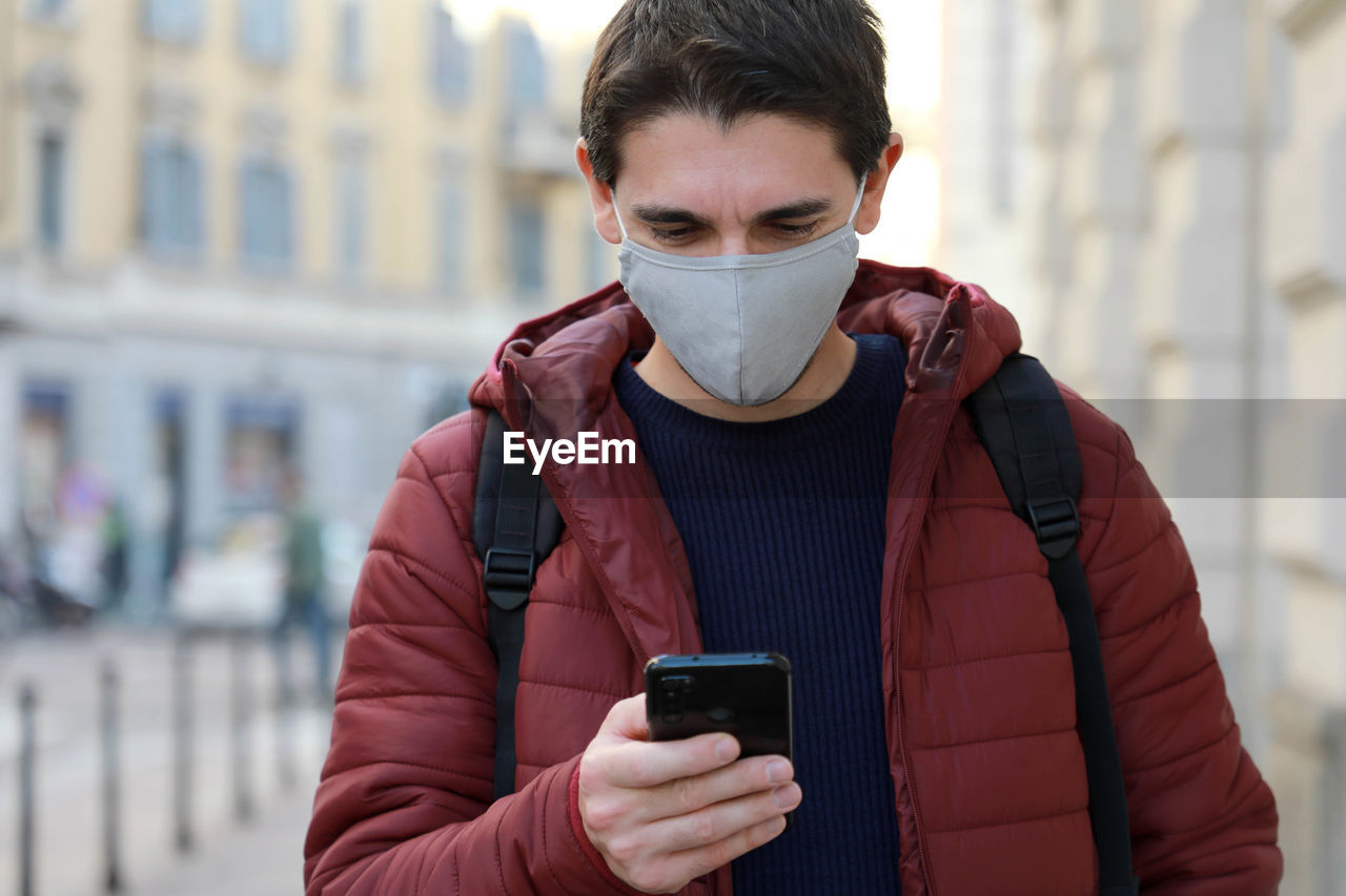 Man wearing mask using phone while standing outdoors
