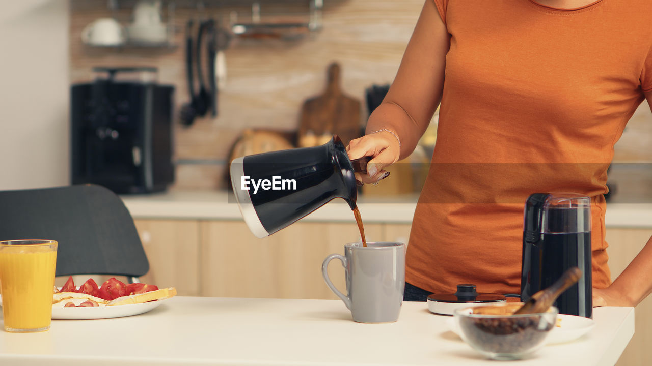Woman pouring coffee in cup at home