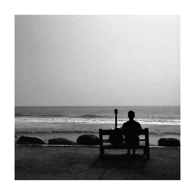 Silhouette of man with acoustic guitar sitting in front of sea