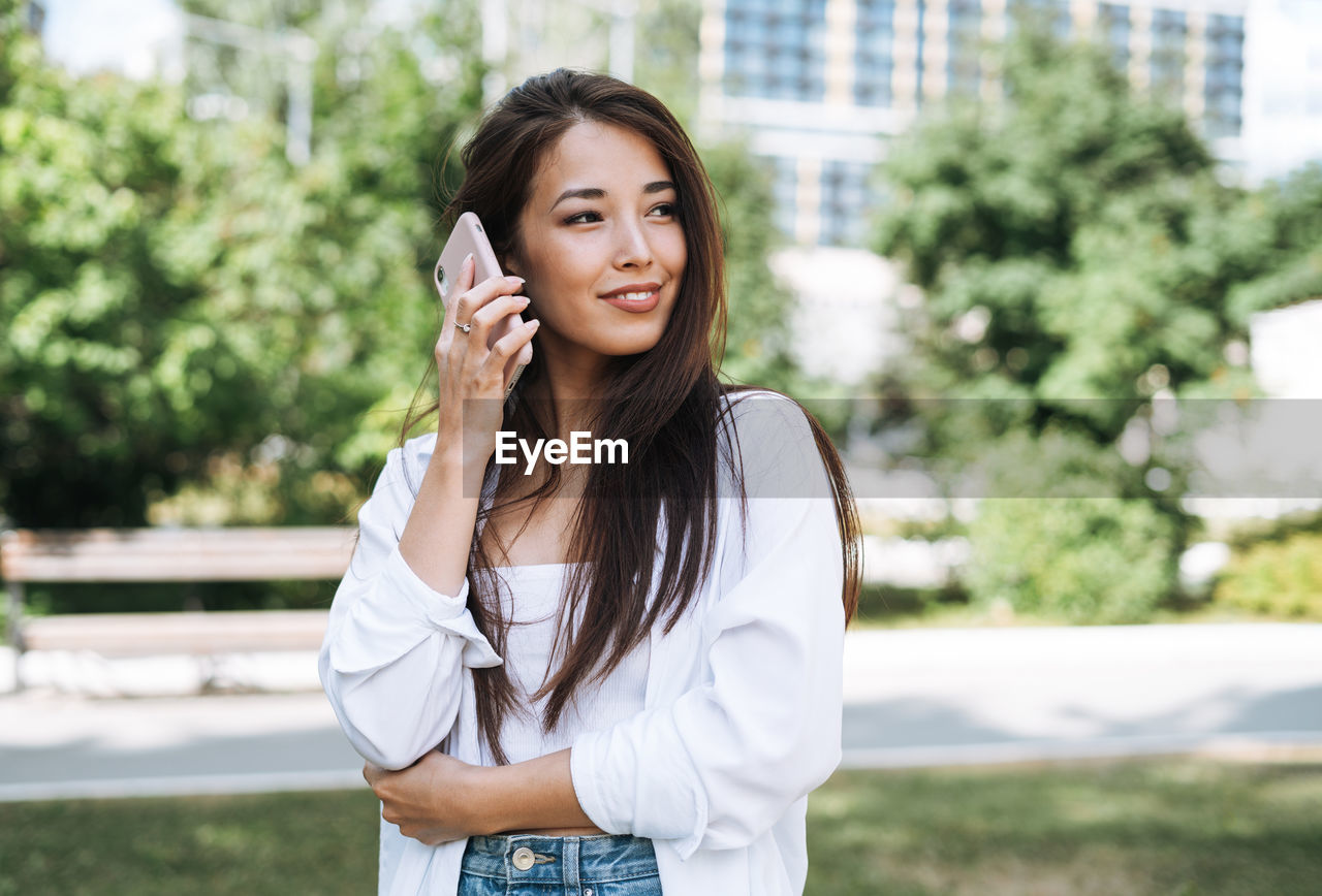 Portrait of young asian woman student with long hair using mobile phone in city park