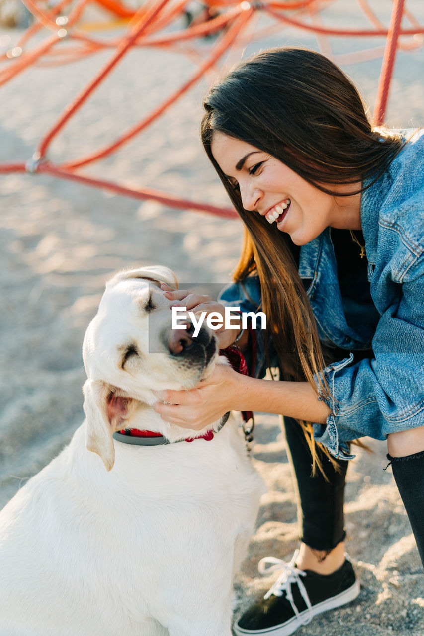 Cheerful woman petting dog at playground during sunset