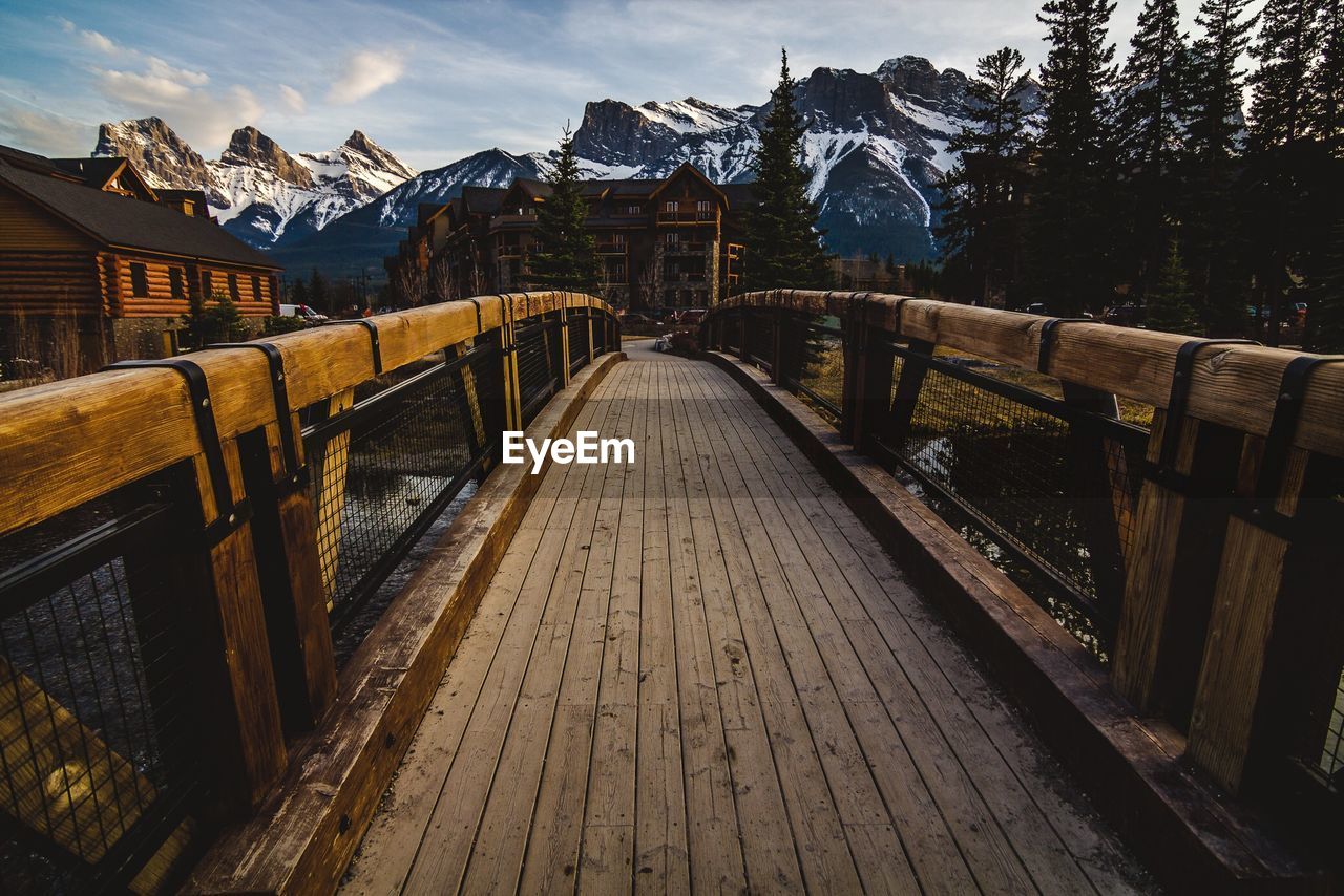 Bridge leading towards snow covered mountains against sky