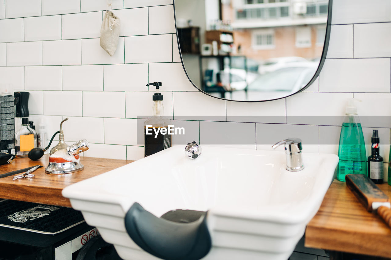 Table with assorted cosmetic products in bottles and dispensers between washstands under mirrors reflecting barbershop