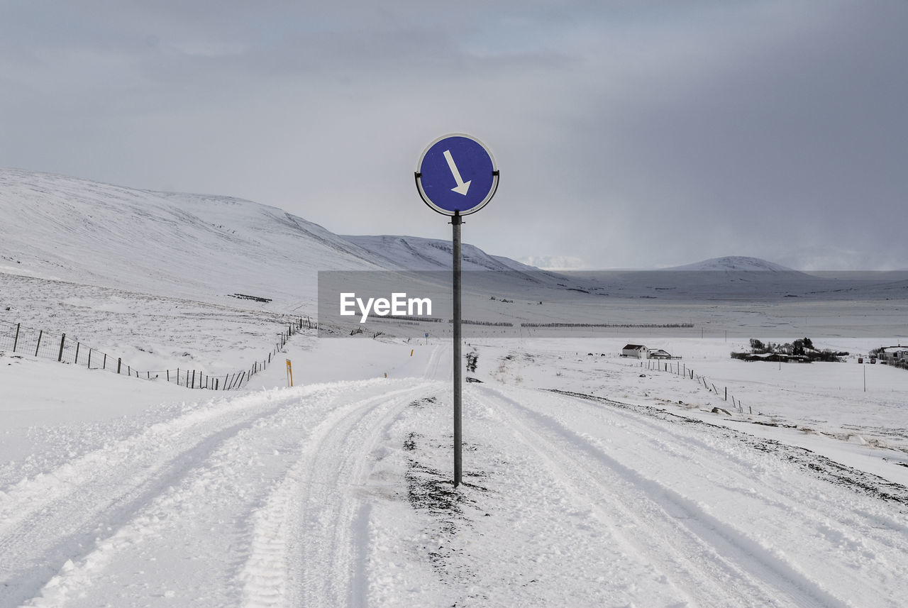 Road sign on snow covered landscape against sky