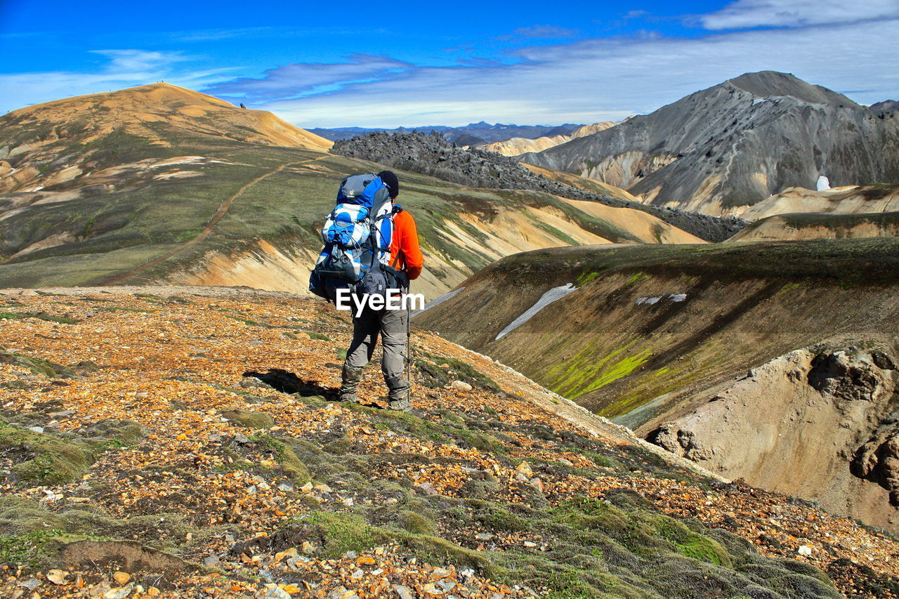 Rear view of hiker with backpack standing on landscape against sky