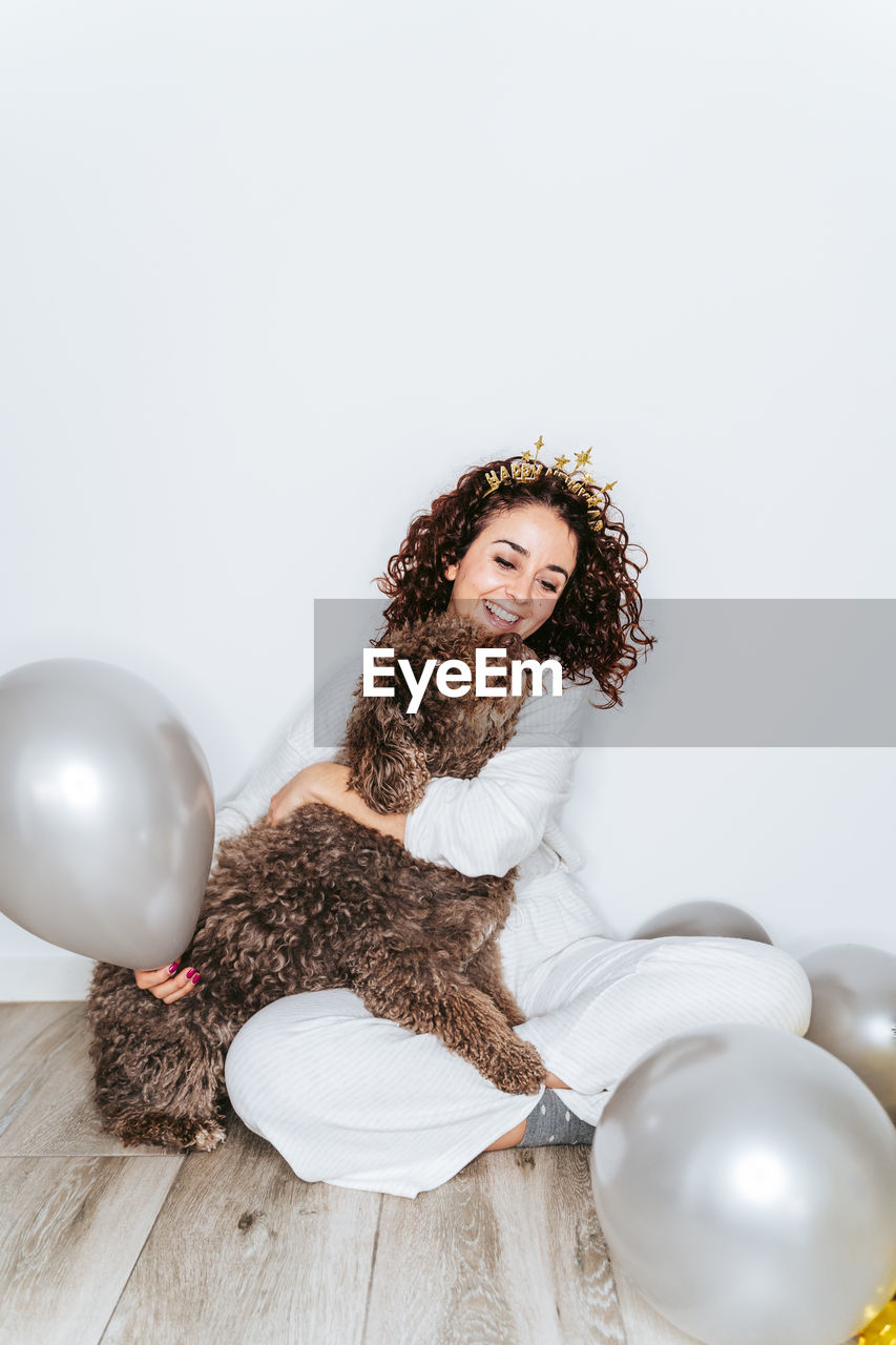 Smiling woman sitting with dog against wall at home